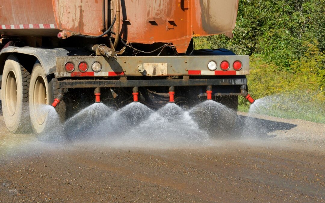 A truck sprays dust suppressant on a dirt road to control dust.
