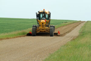 A tractor grades a dirt road to prepare it for an application of dust suppressant. 